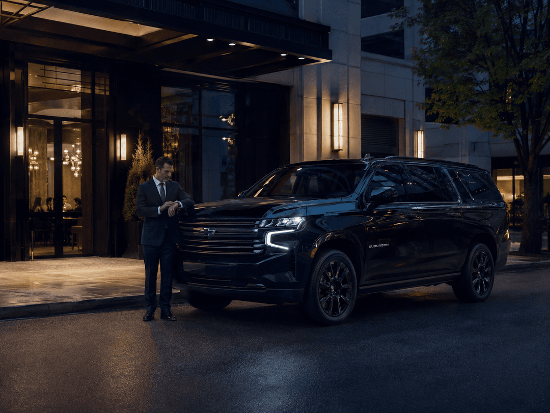 Professional chauffeur waiting beside a black Chevrolet Suburban