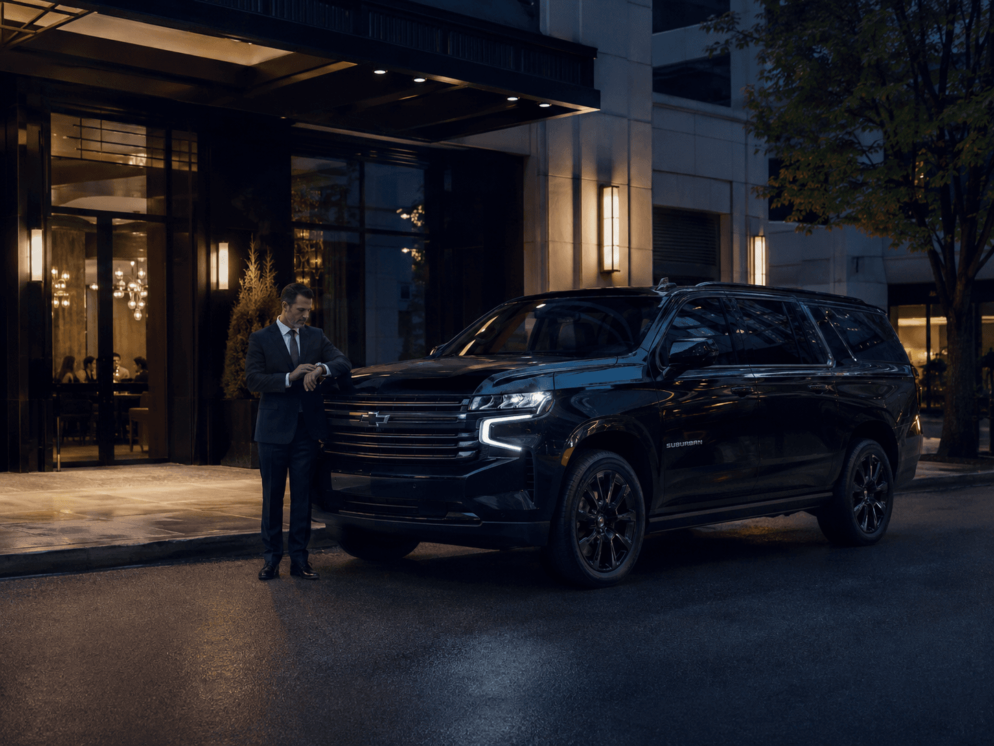 Professional chauffeur waiting beside a black Chevrolet Suburban